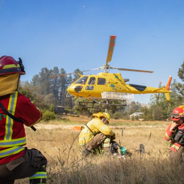 Brigadistas forestales coordinan operaciones junto a un helicóptero durante el combate de incendios forestales en el Maule.