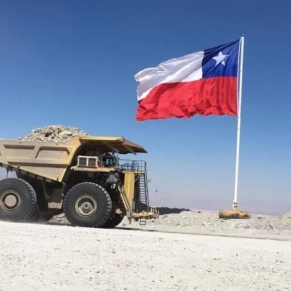 Camión minero circula junto a una bandera chilena en una faena minera.