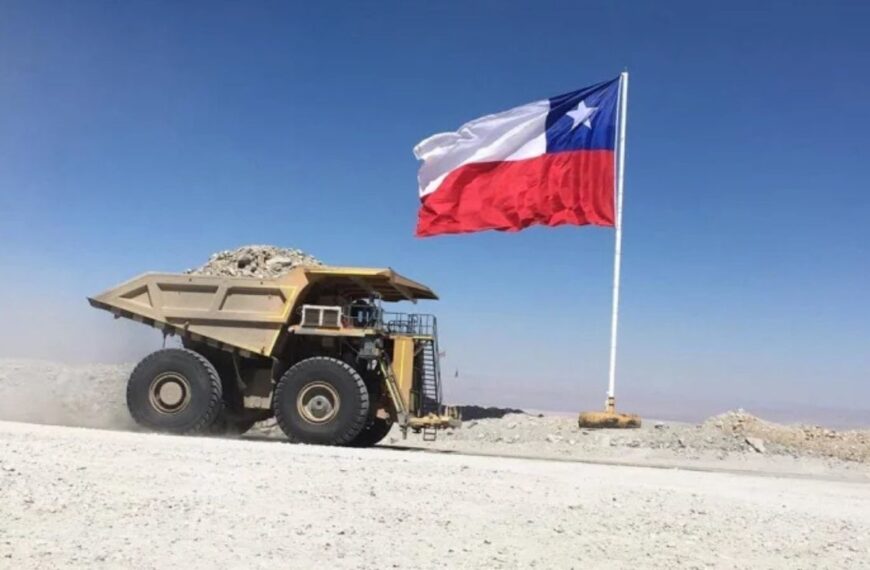 Camión minero circula junto a una bandera chilena en una faena minera.