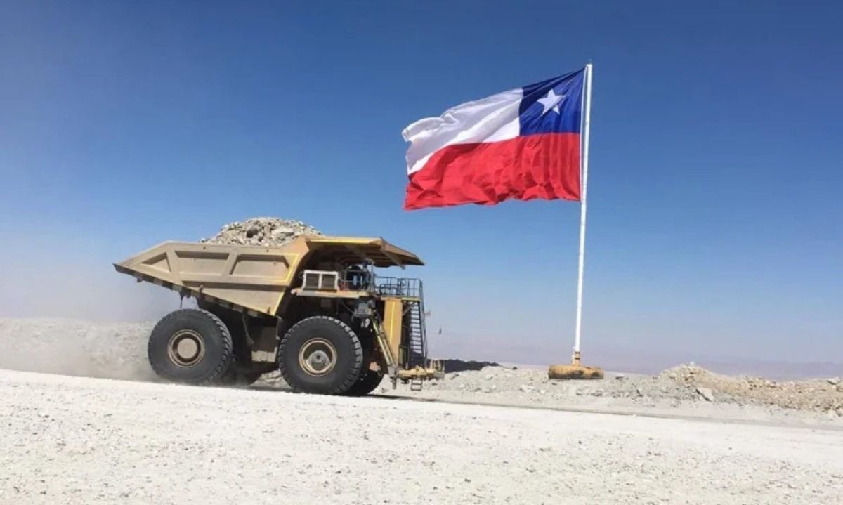 Camión minero circula junto a una bandera chilena en una faena minera.