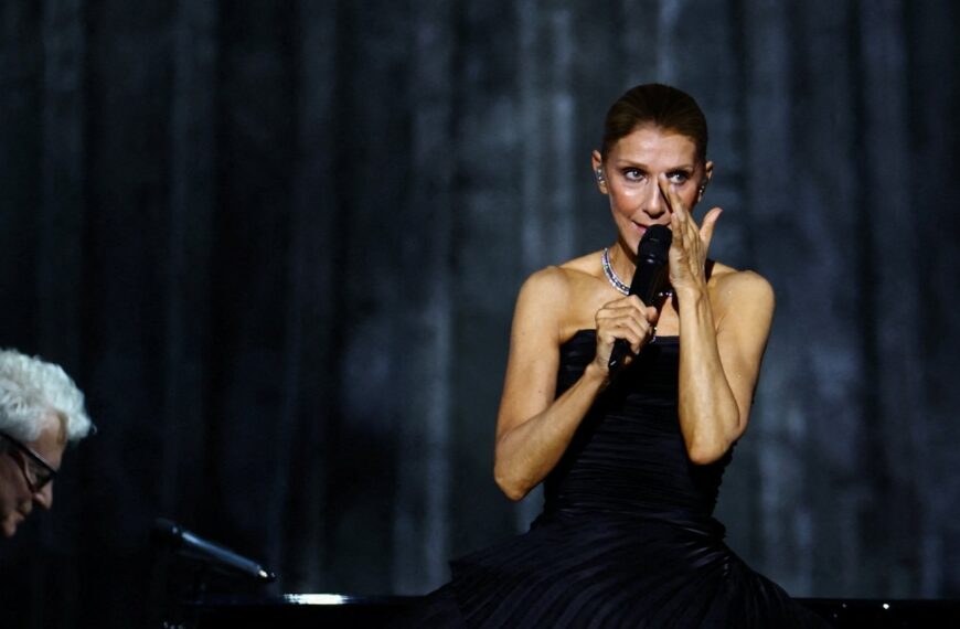 Celine Dion se seca una lágrima mientras sostiene un micrófono durante una presentación.