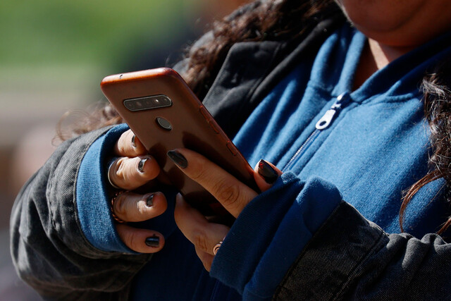 Joven utiliza un teléfono celular con ambas manos.