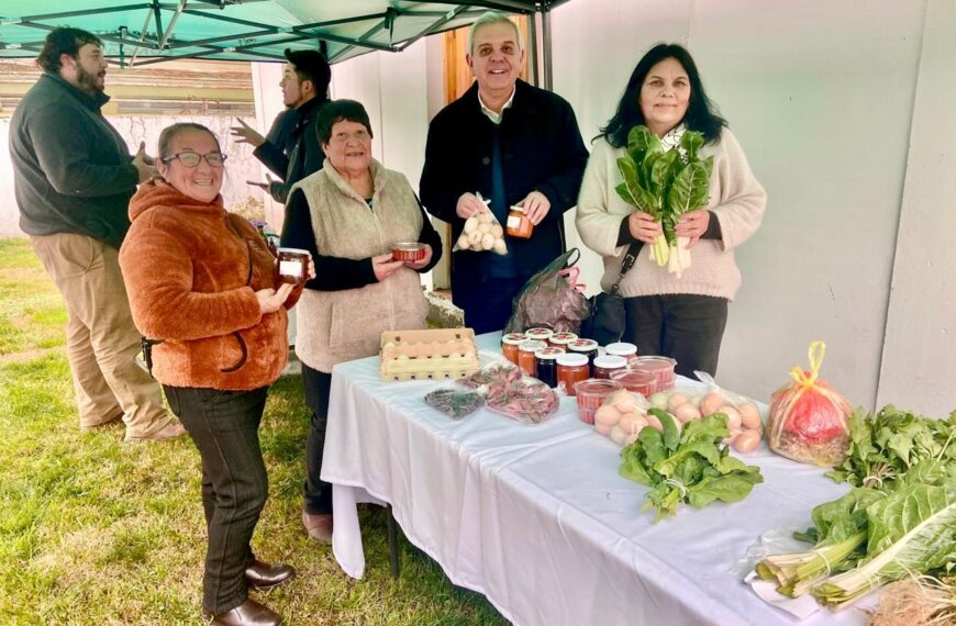 Mujeres y representantes locales posan junto a una mesa con hortalizas, huevos, conservas y otros productos rurales.