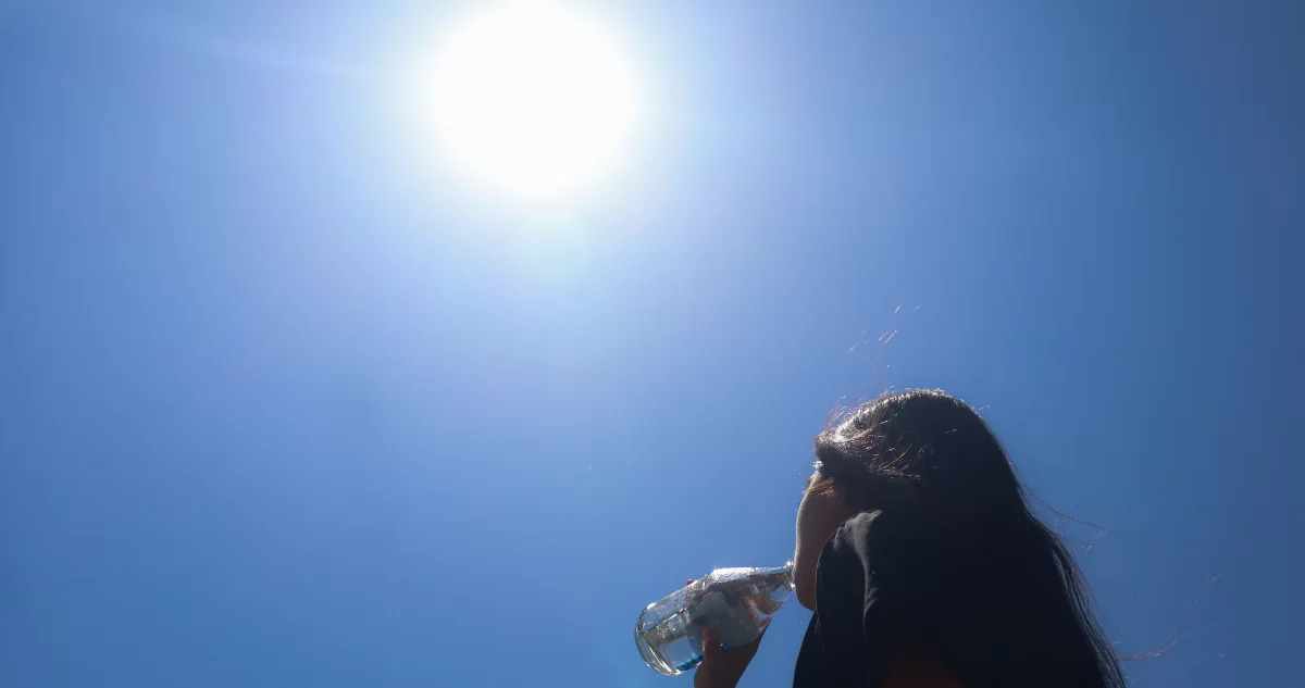 Mujer bebe agua bajo el sol en un día de altas temperaturas.