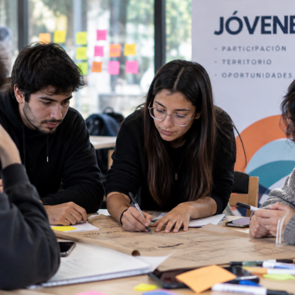 Jóvenes trabajan en grupo alrededor de una mesa mientras escriben y organizan ideas para un proyecto.