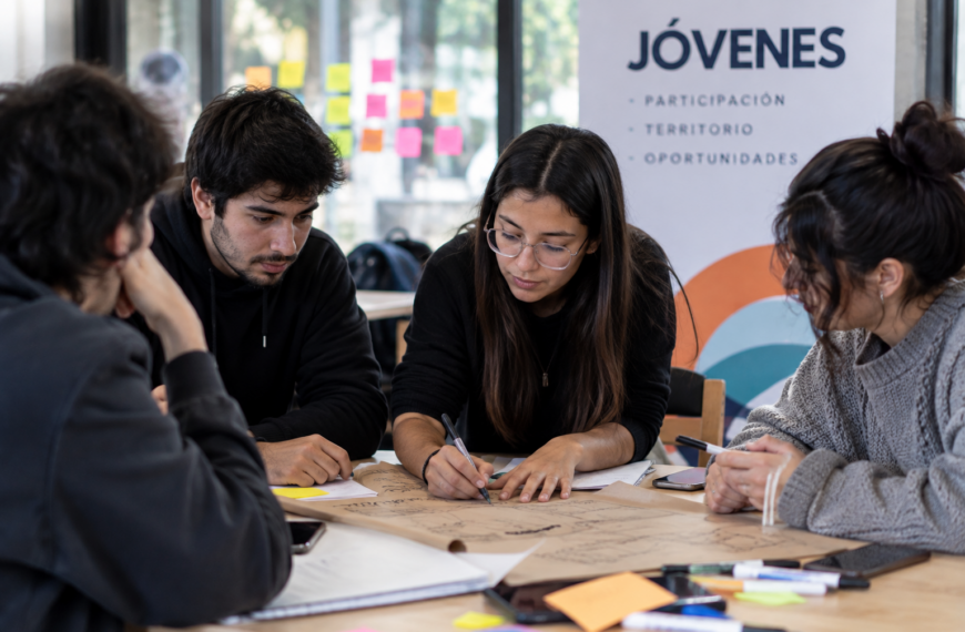 Jóvenes trabajan en grupo alrededor de una mesa mientras escriben y organizan ideas para un proyecto.
