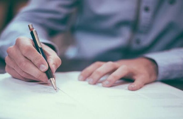 Persona firma un documento con un lápiz sobre una mesa.